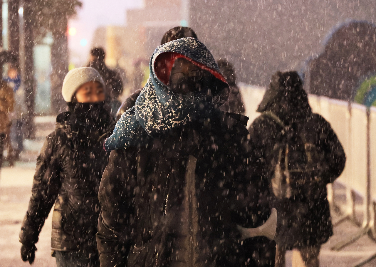Commuters walk through central Seoul on Thursday as the first snow of the season falls. (Yonhap)